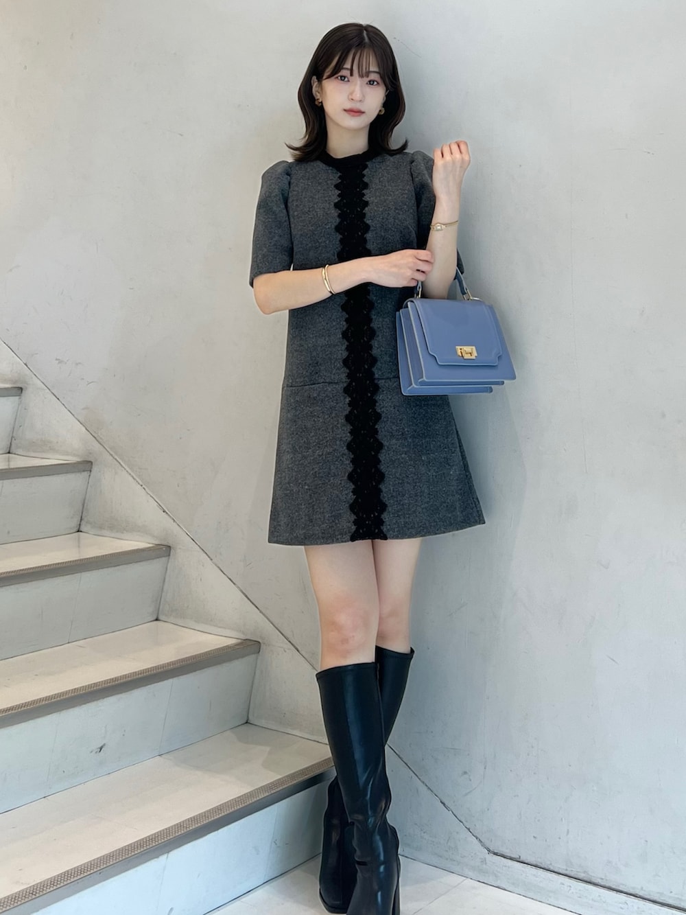 グレー系のワンピース、ブラック系のブーツ、ブルー系のハンドバッグを着用したレディースの秋コーディネートの7枚目の写真