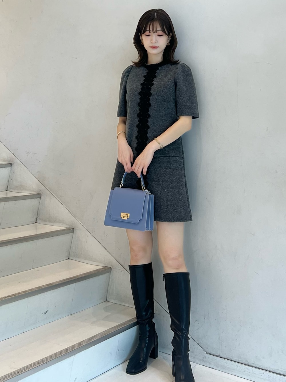 グレー系のワンピース、ブラック系のブーツ、ブルー系のハンドバッグを着用したレディースの秋コーディネートの2枚目の写真