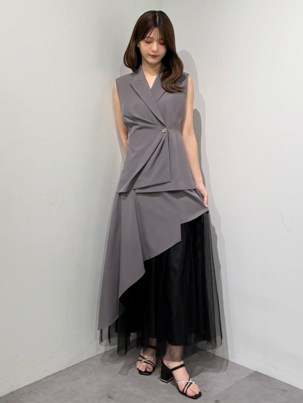 グレー系のベスト、グレー系のスカート、ブラック系のサンダルを着用したレディースの春コーディネートの3枚目の写真