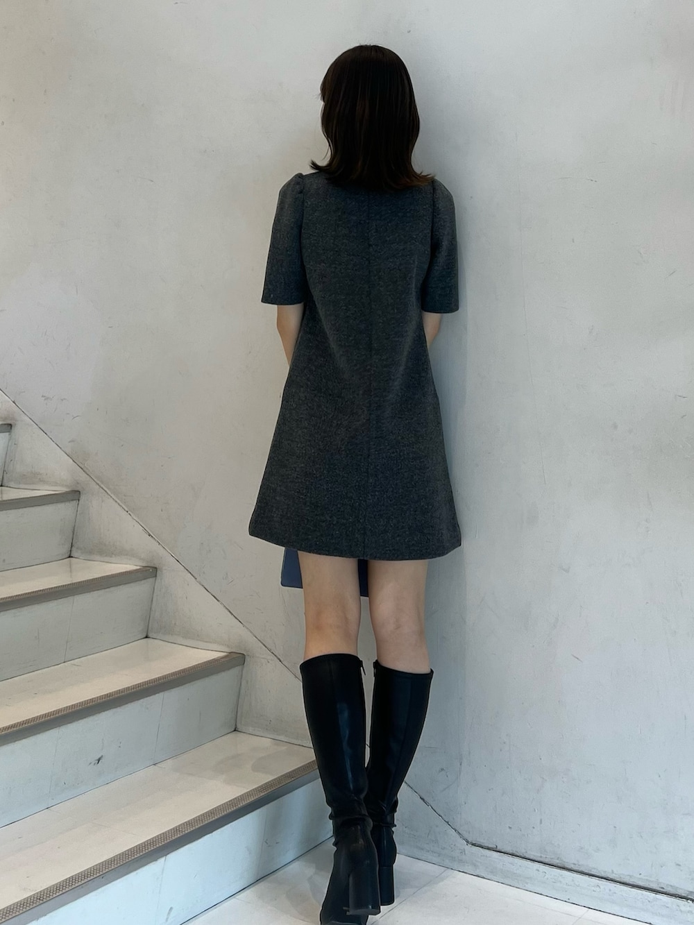 グレー系のワンピース、ブラック系のブーツ、ブルー系のハンドバッグを着用したレディースの秋コーディネートの4枚目の写真