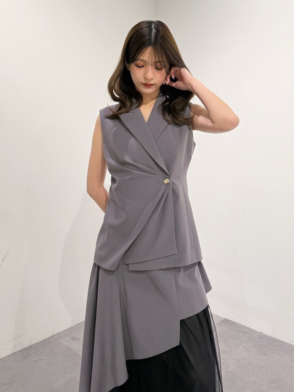 グレー系のベスト、グレー系のスカート、ブラック系のサンダルを着用したレディースの春コーディネートの6枚目の写真