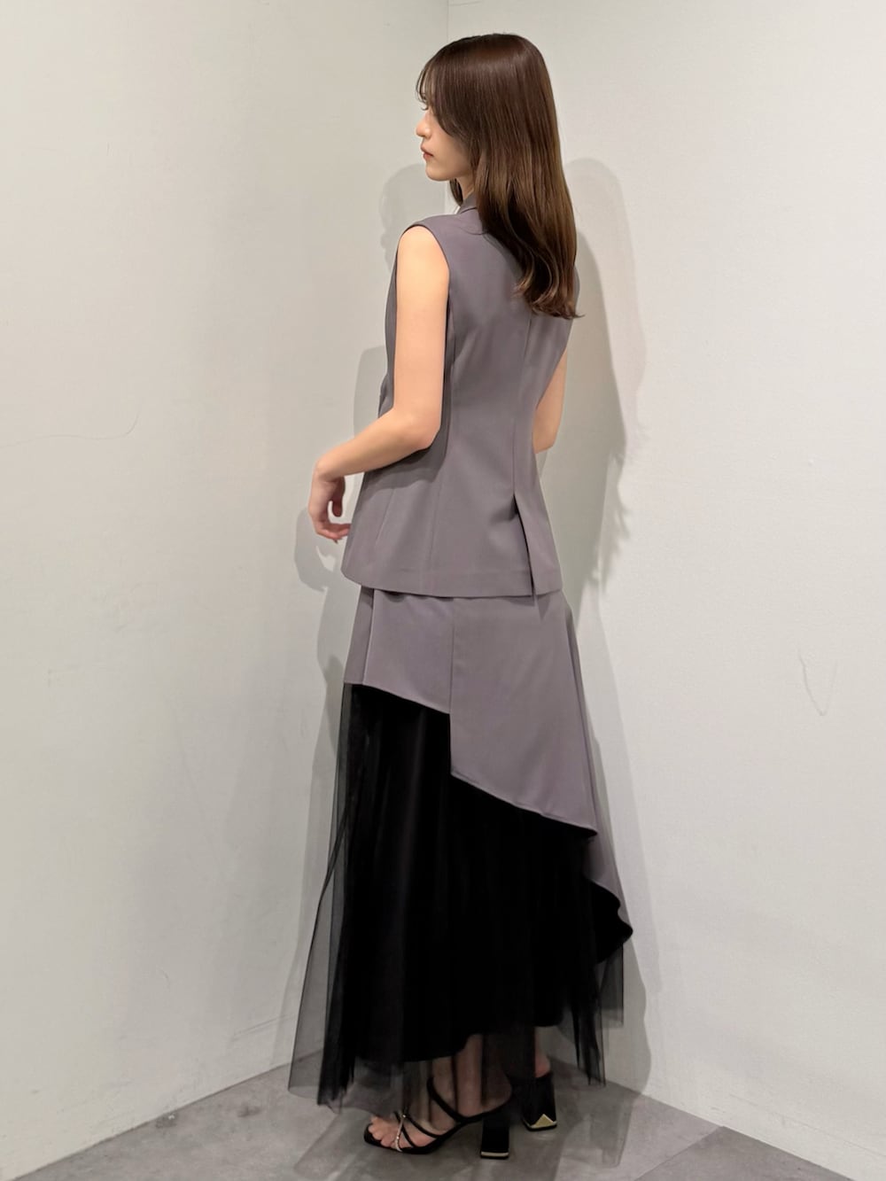 グレー系のベスト、グレー系のスカート、ブラック系のサンダルを着用したレディースの春コーディネートの4枚目の写真