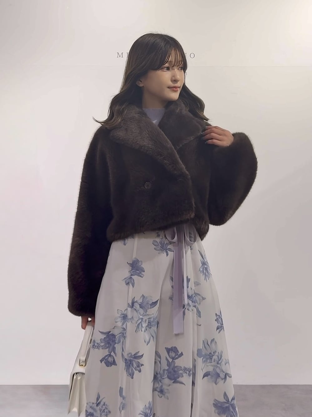 パープル系のワンピース、ブラウン系のブーツ、ホワイト系のハンドバッグを着用したレディースの秋コーディネートの2枚目の写真