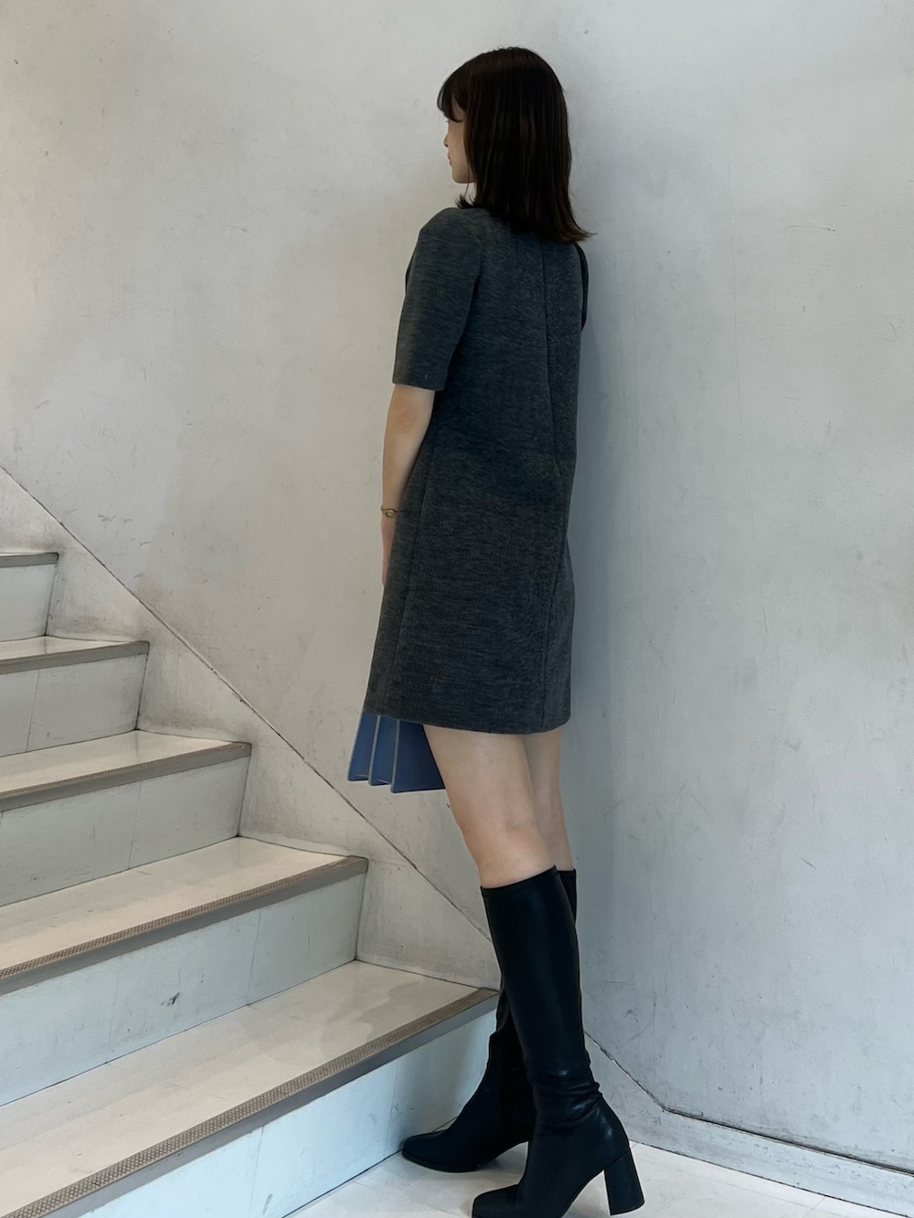 グレー系のワンピース、ブラック系のブーツ、ブルー系のハンドバッグを着用したレディースの秋コーディネートの3枚目の写真