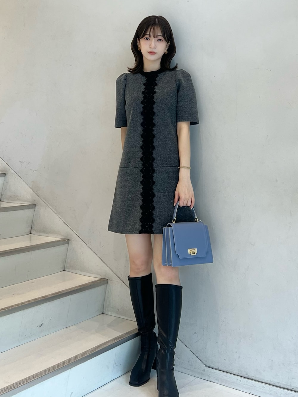 グレー系のワンピース、ブラック系のブーツ、ブルー系のハンドバッグを着用したレディースの秋コーディネートの5枚目の写真