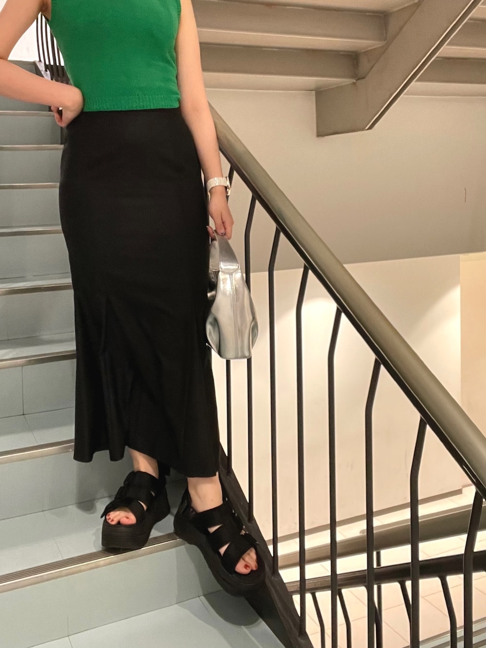 ブラック系のスカート、グリーン系のタンクトップ、ブラック系のサンダルを着用したレディースの春コーディネートの4枚目の写真