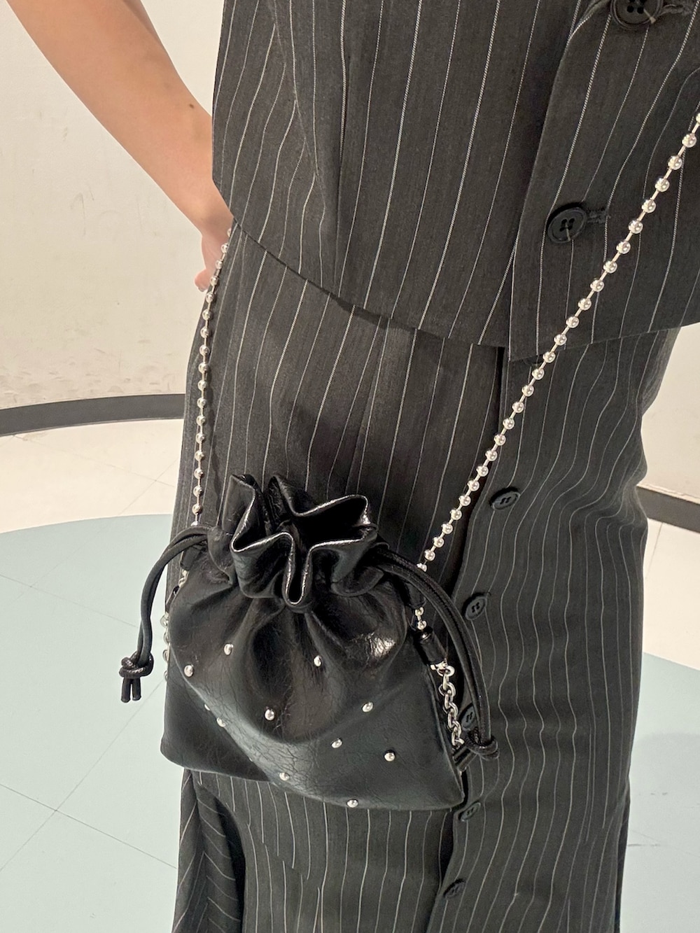 ブラック系のショルダーバッグ、ブラック系のサンダル、グレー系のジャンパースカートを着用したレディースの夏コーディネートの4枚目の写真