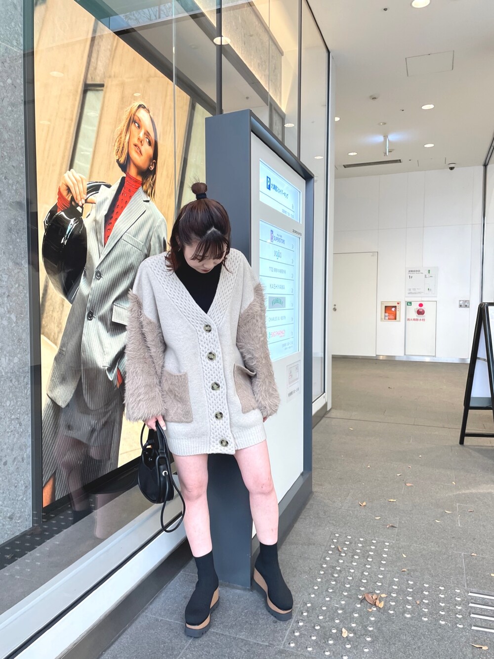 ベージュ系のカーディガン/ボレロ、ブラック系のブーツ、ブラック系のハンドバッグを着用したレディースの秋コーディネートの2枚目の写真