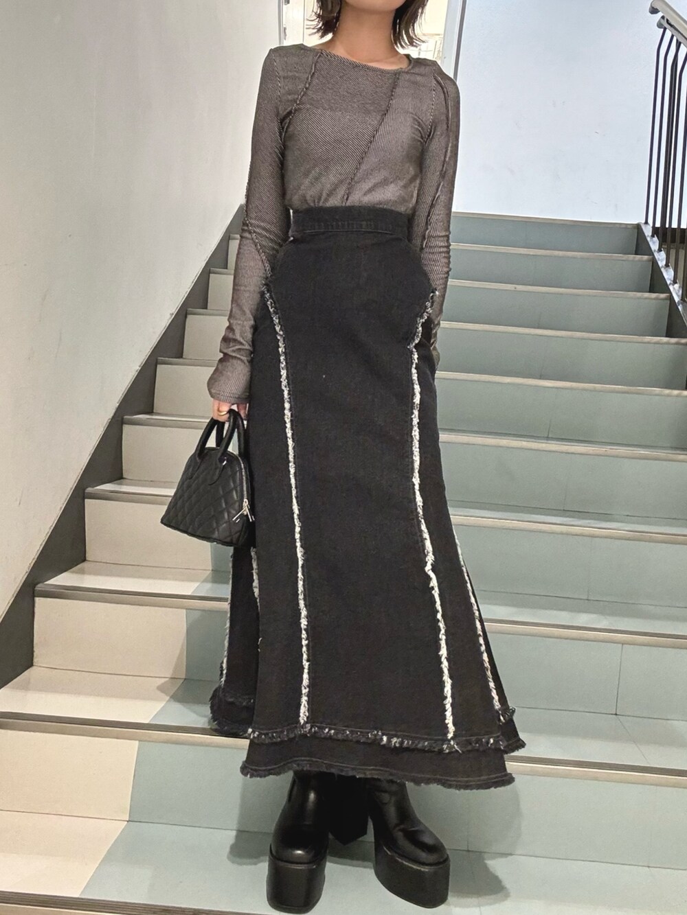 ブラック系のデニムスカート、グレー系のTシャツ/カットソー、ブラック系のハンドバッグを着用したレディースの冬コーディネートの5枚目の写真