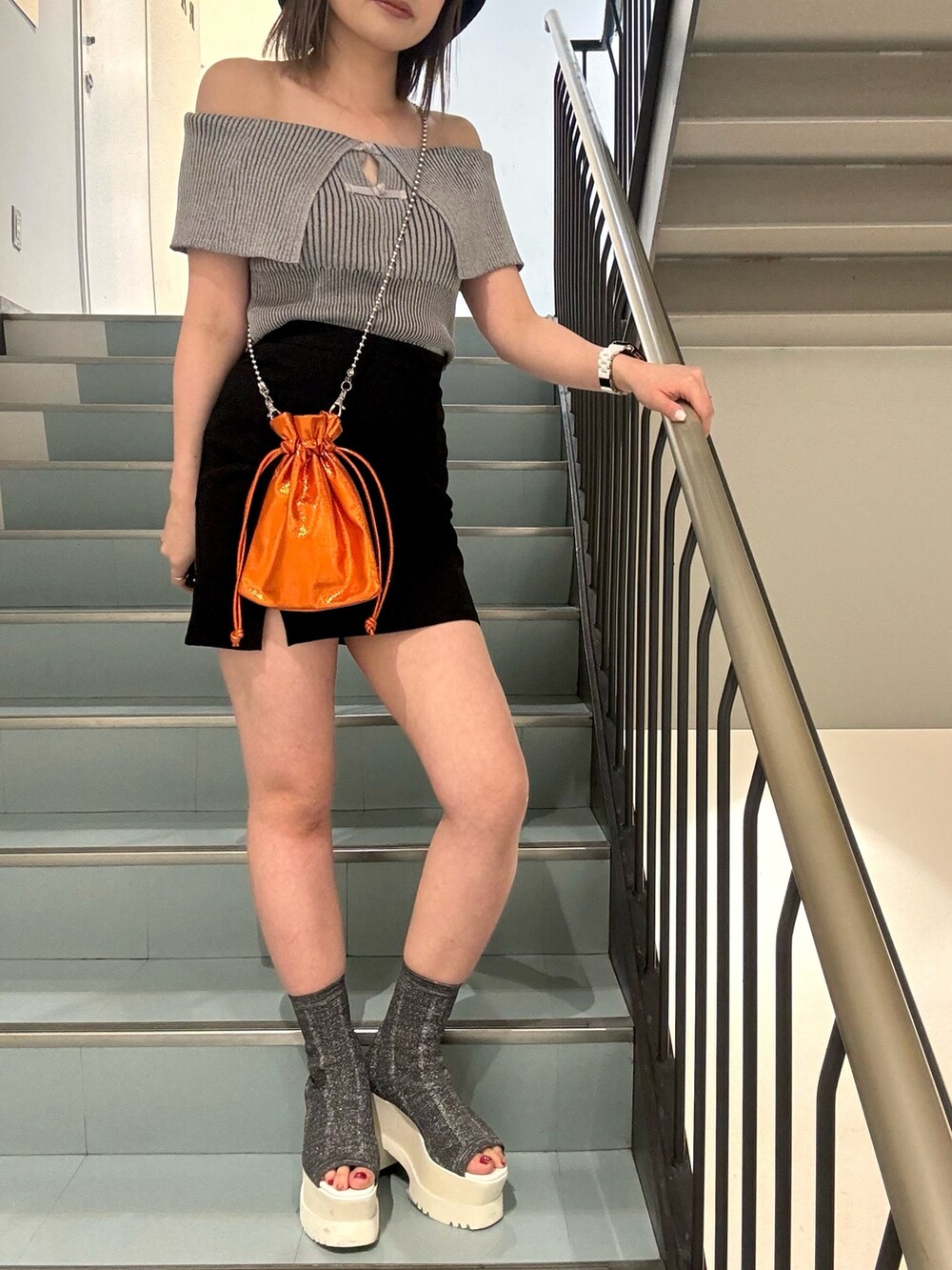 グレー系のニット/セーター、ブラック系のスカート、オレンジ系のショルダーバッグを着用したレディースの春コーディネートの6枚目の写真