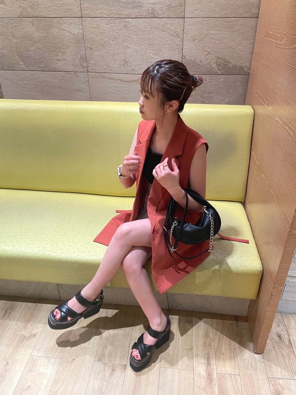 ブラック系のハンドバッグ、ブラック系のサンダル、オレンジ系のベストを着用したレディースの夏コーディネートの4枚目の写真