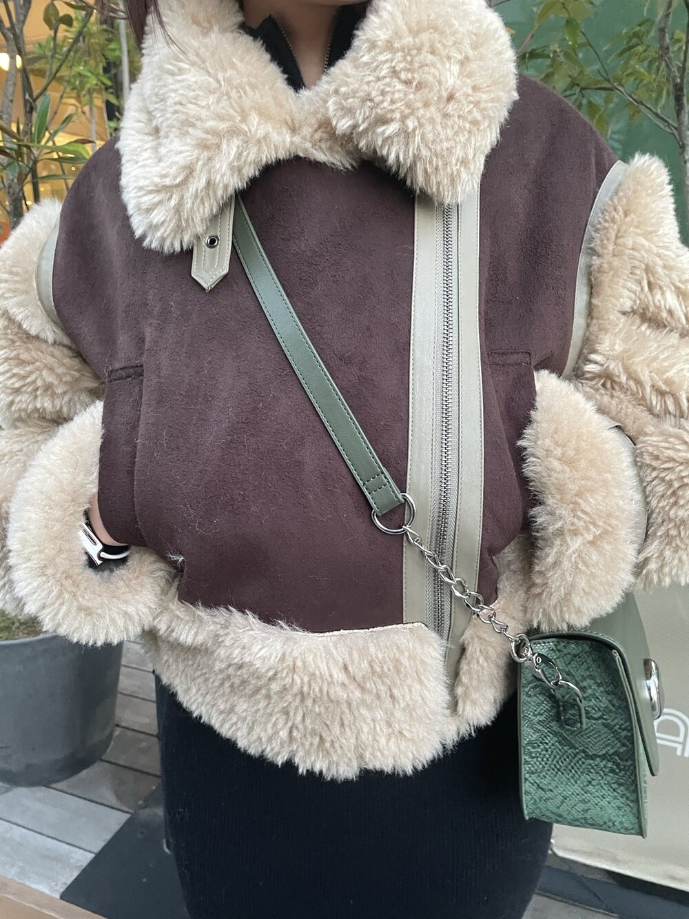 ブラウン系のムートンコート、グリーン系のショルダーバッグ、ブラック系のワンピースを着用したレディースの冬コーディネートの5枚目の写真