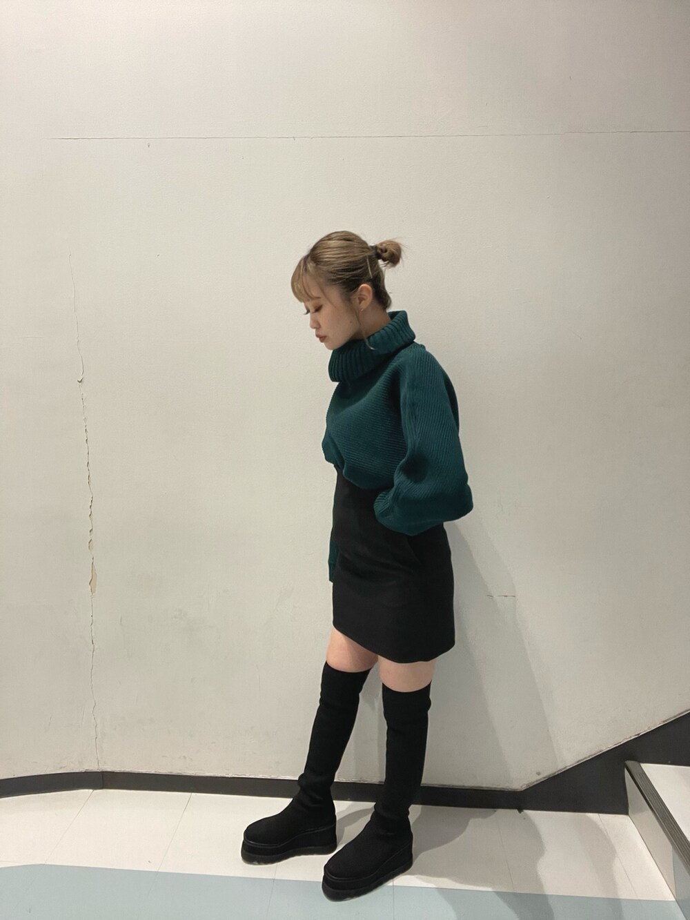 グリーン系のニット/セーター、ブラック系のブーツ、ブラック系のスカートを着用したレディースの秋コーディネートの3枚目の写真