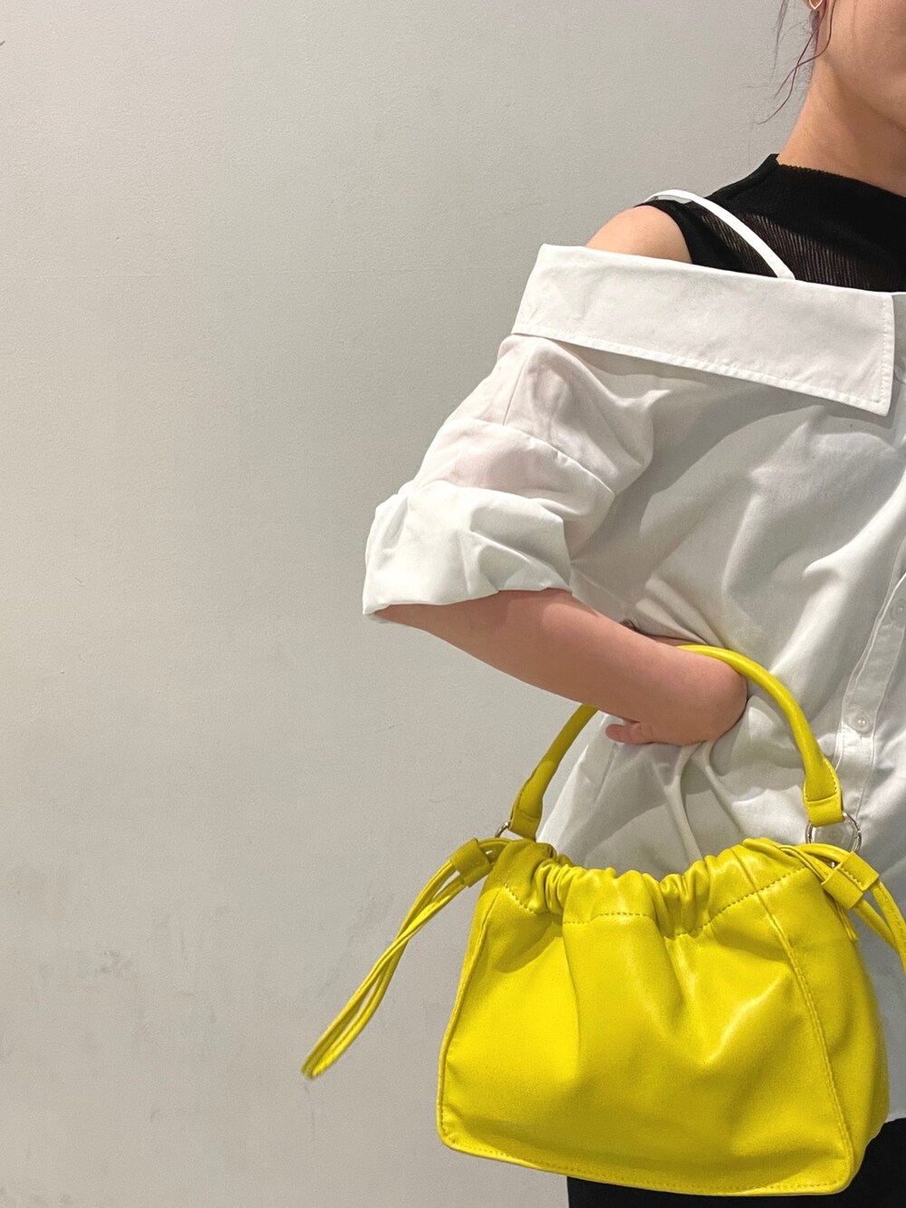 イエロー系のハンドバッグ、ホワイト系のシャツ/ブラウス、ブラック系のブーツを着用したレディースの夏コーディネートの5枚目の写真