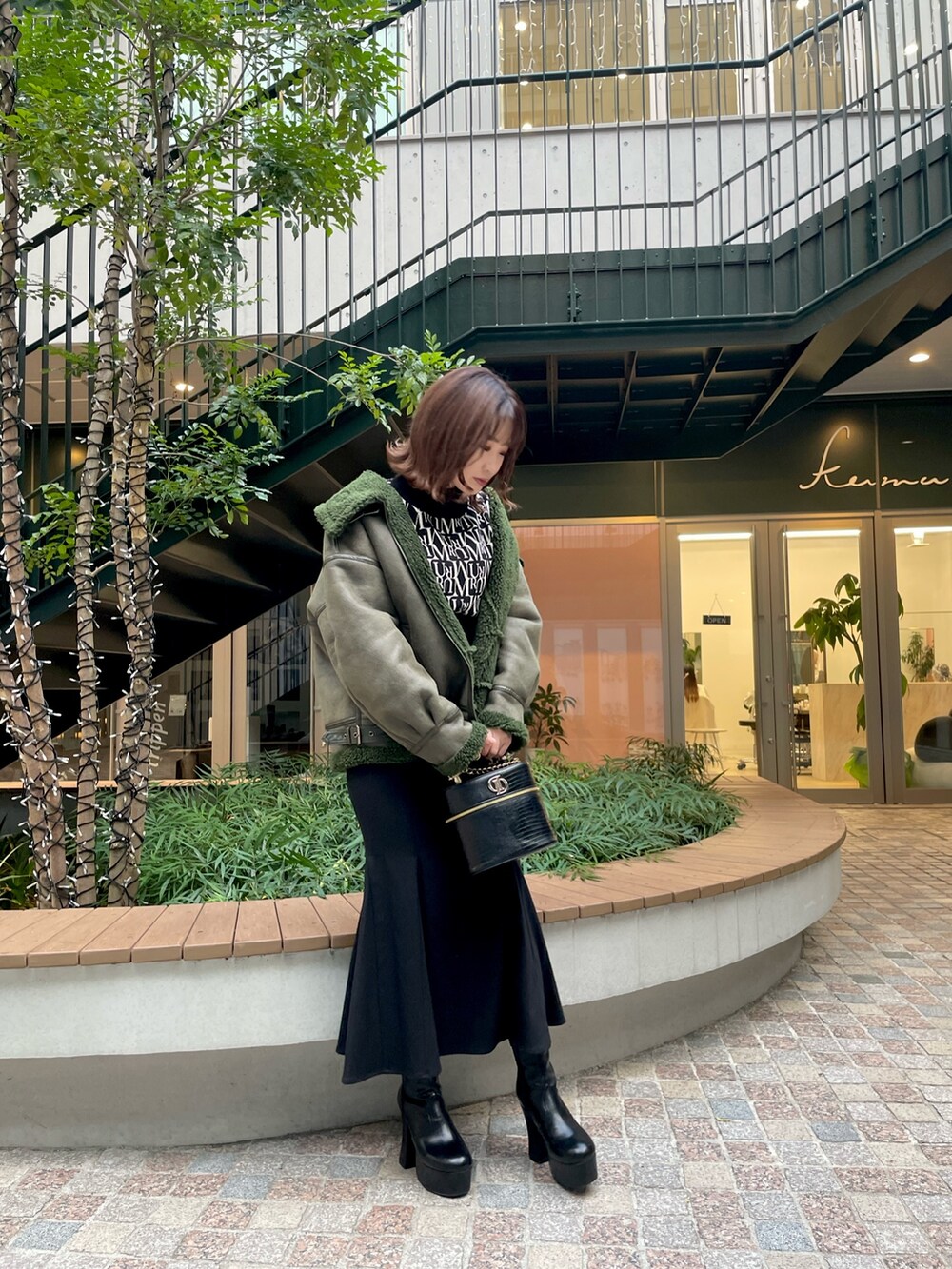 ブラック系のニット/セーター、ブラック系のスカート、グリーン系のムートンコートを着用したレディースの秋コーディネートの2枚目の写真
