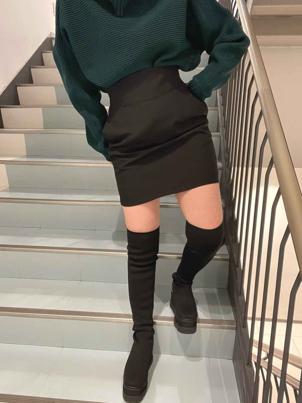 グリーン系のニット/セーター、ブラック系のブーツ、ブラック系のスカートを着用したレディースの秋コーディネートの6枚目の写真