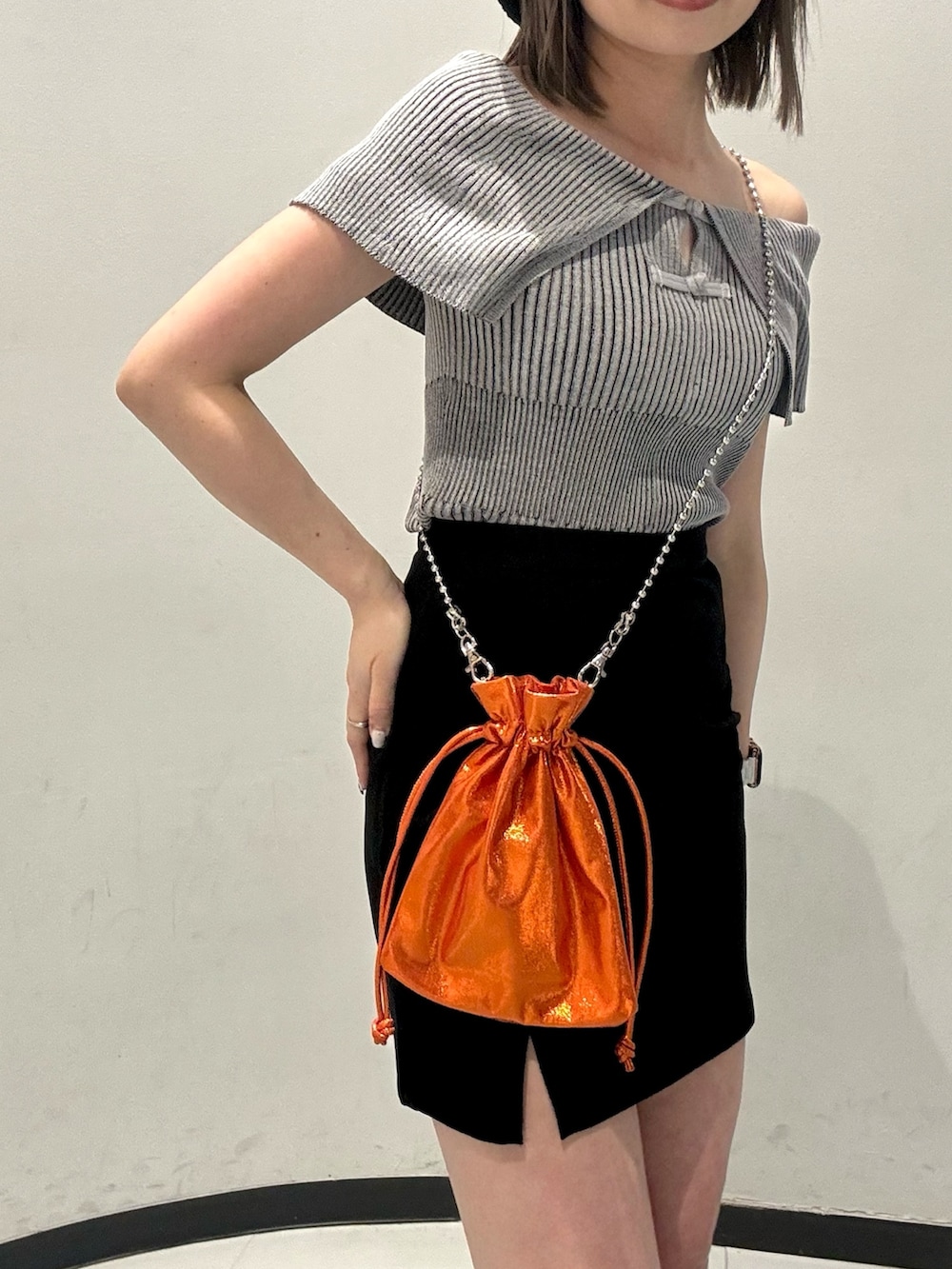 グレー系のニット/セーター、ブラック系のスカート、オレンジ系のショルダーバッグを着用したレディースの春コーディネートの5枚目の写真