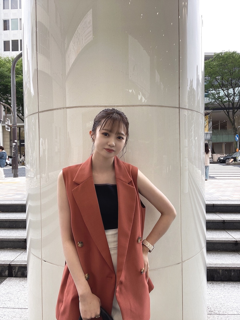 ブラック系のハンドバッグ、ブラック系のサンダル、オレンジ系のベストを着用したレディースの夏コーディネートの2枚目の写真