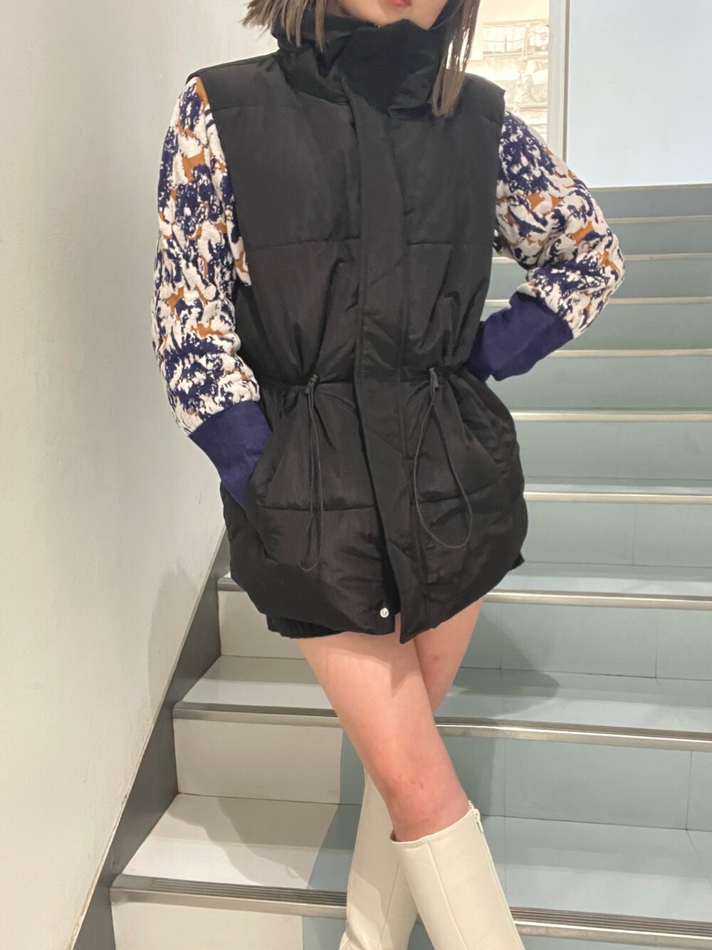 グリーン系のハンドバッグ、ブラック系のダウンベスト、ホワイト系のブーツを着用したレディースの秋コーディネートの7枚目の写真