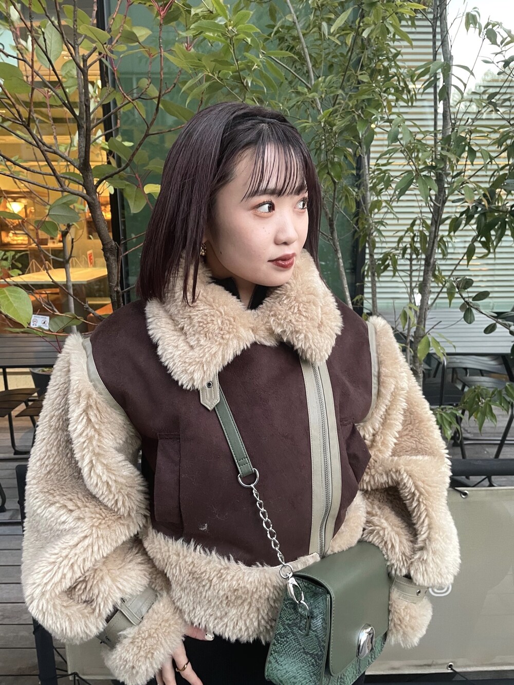 ブラウン系のムートンコート、グリーン系のショルダーバッグ、ブラック系のワンピースを着用したレディースの冬コーディネートの2枚目の写真