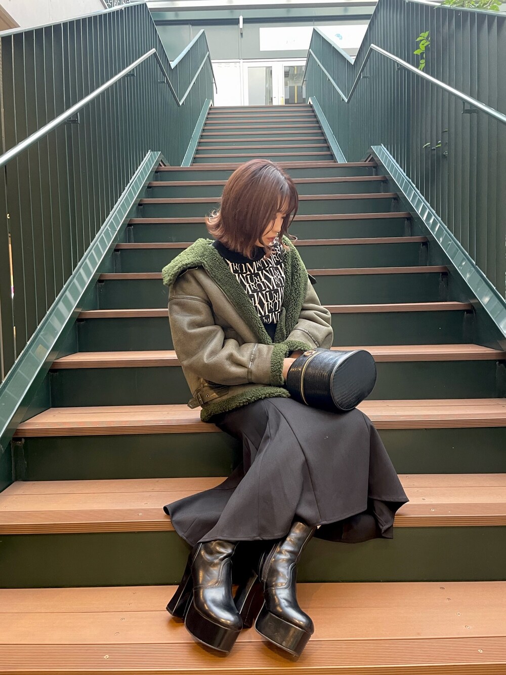 ブラック系のニット/セーター、ブラック系のスカート、グリーン系のムートンコートを着用したレディースの秋コーディネートの3枚目の写真