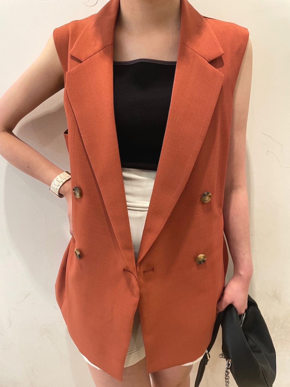 ブラック系のハンドバッグ、ブラック系のサンダル、オレンジ系のベストを着用したレディースの夏コーディネートの5枚目の写真