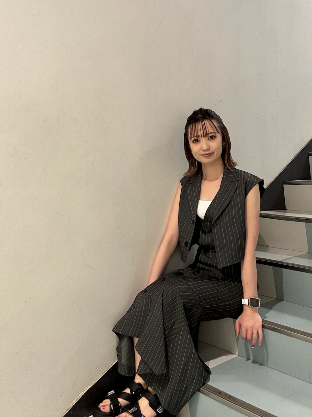 ブラック系のショルダーバッグ、ブラック系のサンダル、グレー系のジャンパースカートを着用したレディースの夏コーディネートの6枚目の写真