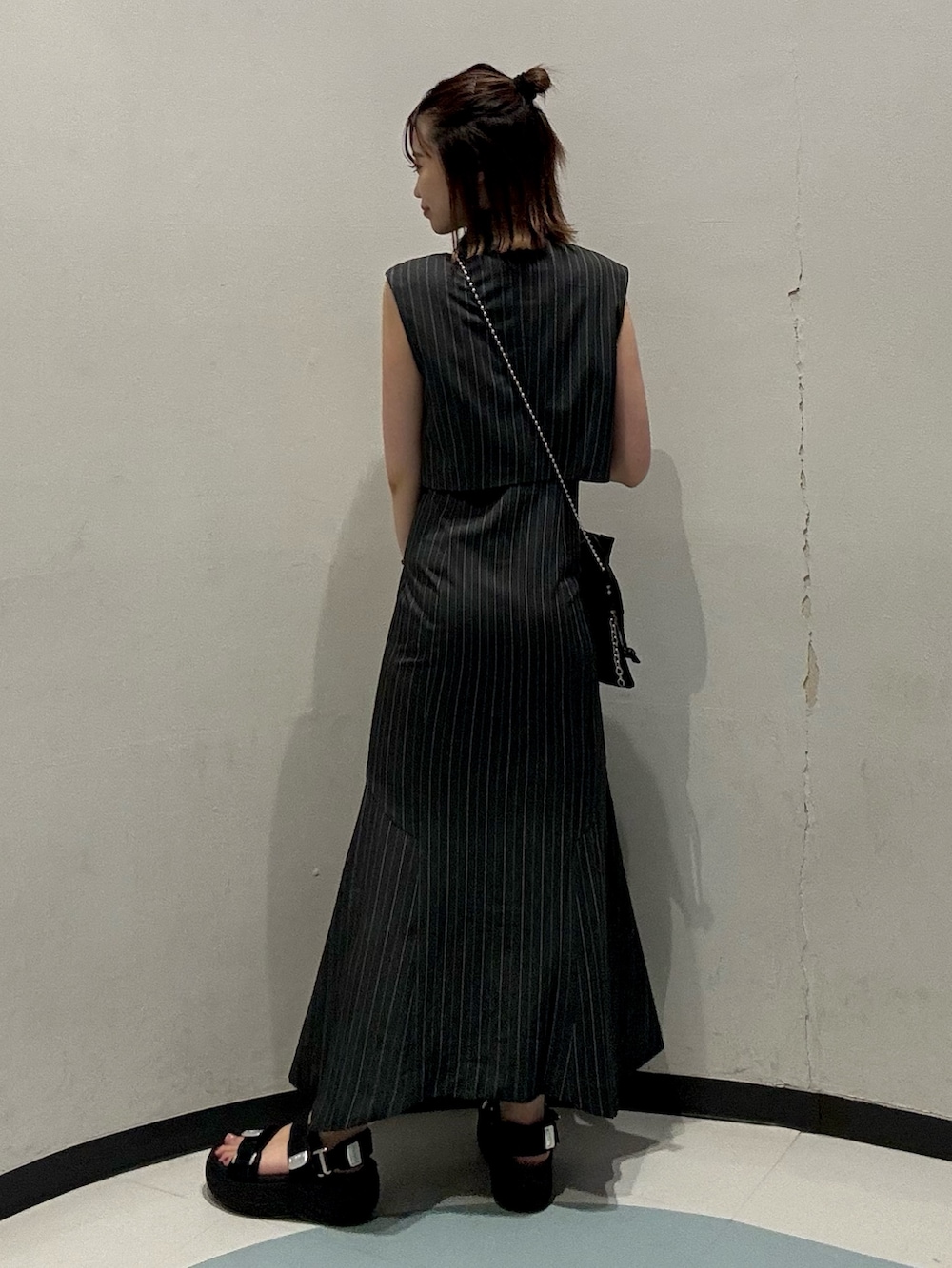 ブラック系のショルダーバッグ、ブラック系のサンダル、グレー系のジャンパースカートを着用したレディースの夏コーディネートの3枚目の写真