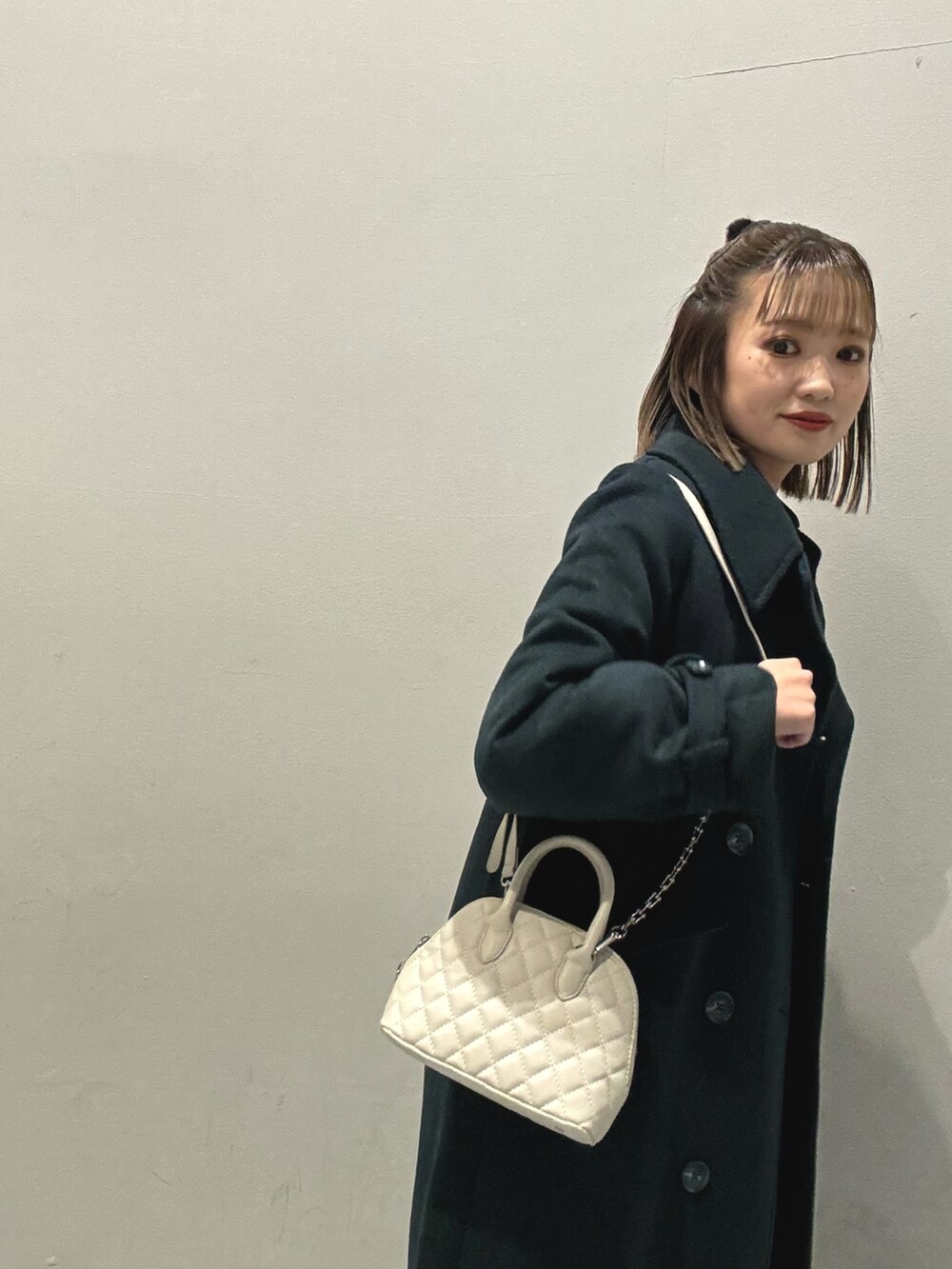 ホワイト系のハンドバッグ、ブラック系のワンピース、グリーン系のチェスターコートを着用したレディースの冬コーディネートの6枚目の写真