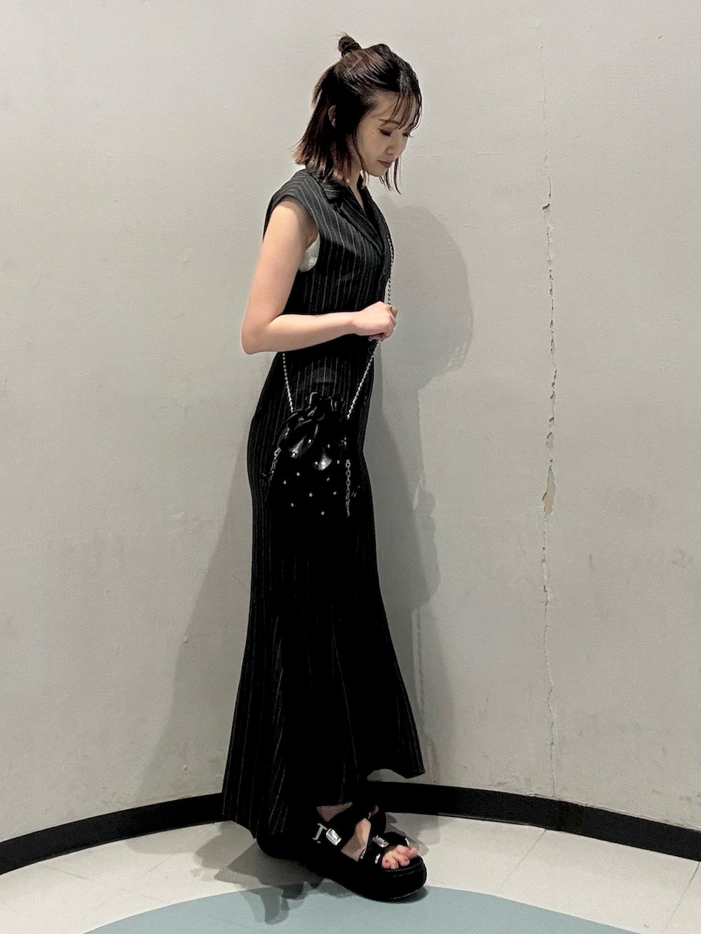 ブラック系のショルダーバッグ、ブラック系のサンダル、グレー系のジャンパースカートを着用したレディースの夏コーディネートの2枚目の写真