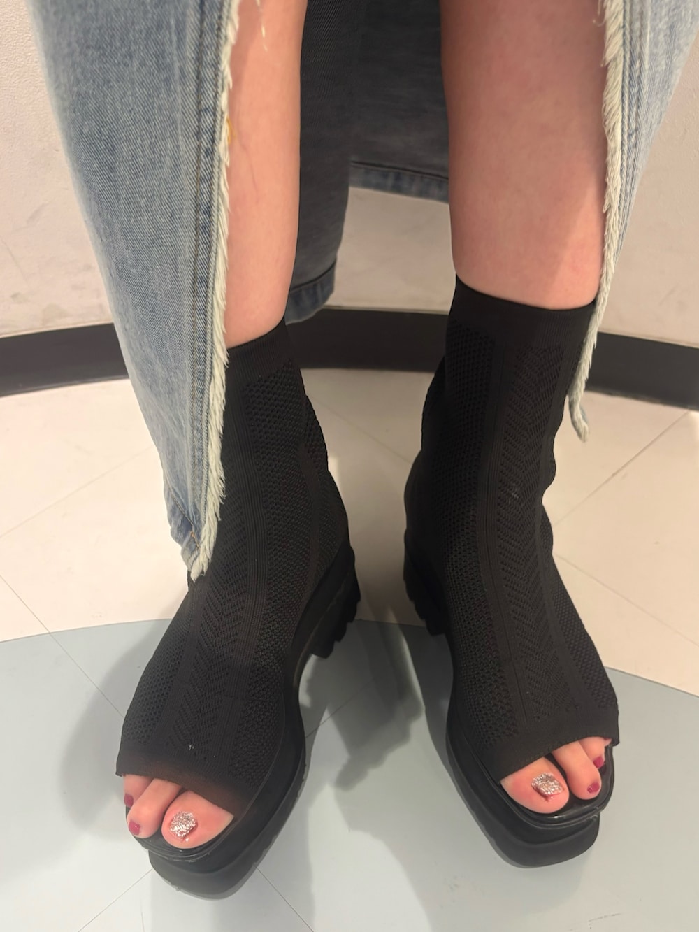 ブラック系のニット/セーター、ブルー系のデニムスカート、ブラック系のサンダルを着用したレディースの夏コーディネートの7枚目の写真