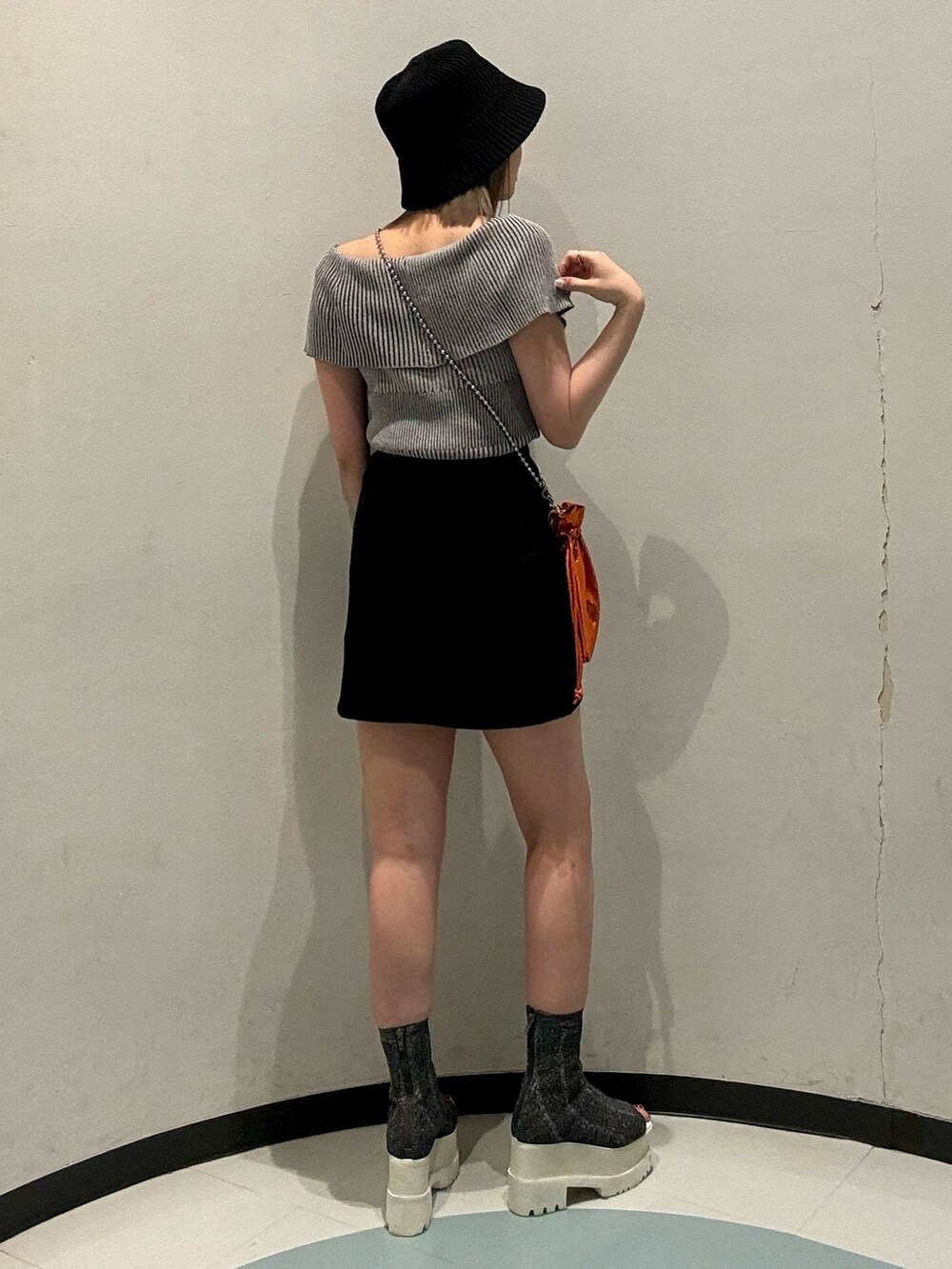 グレー系のニット/セーター、ブラック系のスカート、オレンジ系のショルダーバッグを着用したレディースの春コーディネートの3枚目の写真