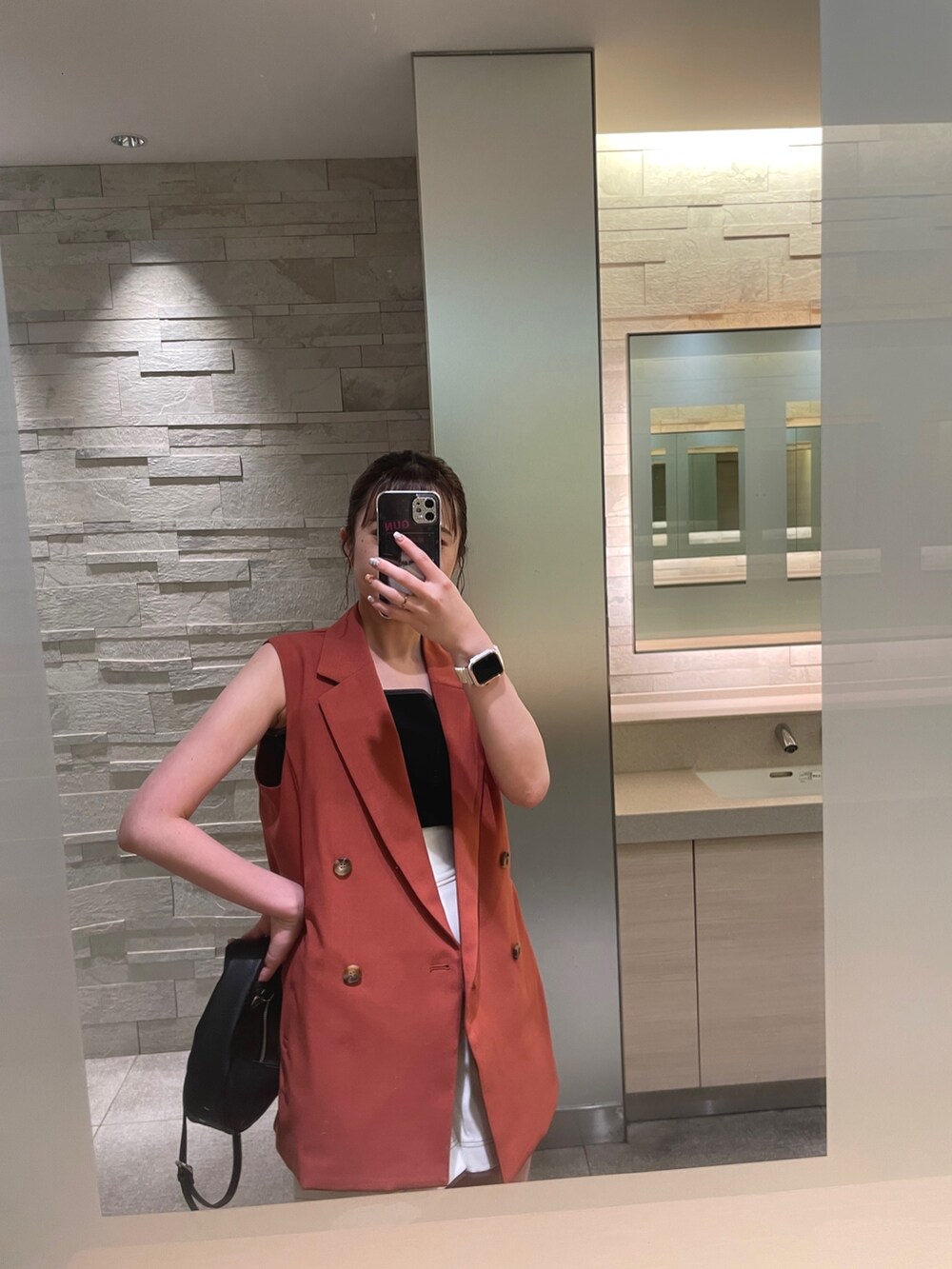 ブラック系のハンドバッグ、ブラック系のサンダル、オレンジ系のベストを着用したレディースの夏コーディネートの3枚目の写真