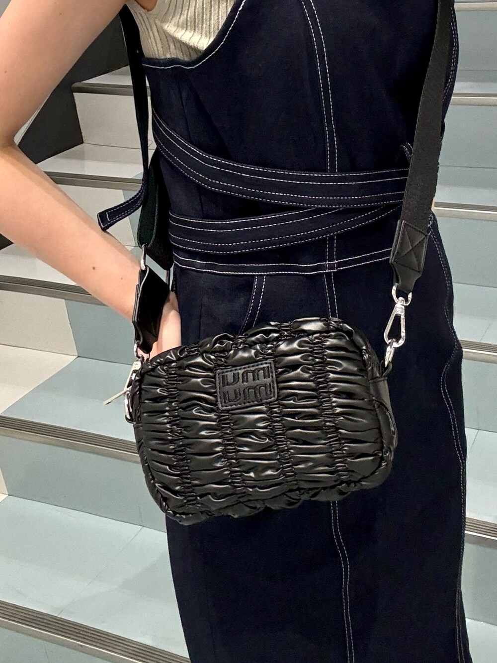 ベージュ系のニット/セーター、ブルー系のジャンパースカート、ブラック系のショルダーバッグを着用したレディースの春コーディネートの6枚目の写真