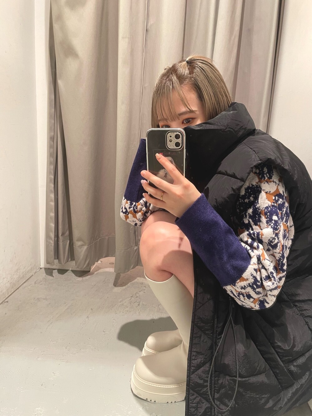 グリーン系のハンドバッグ、ブラック系のダウンベスト、ホワイト系のブーツを着用したレディースの秋コーディネートの5枚目の写真