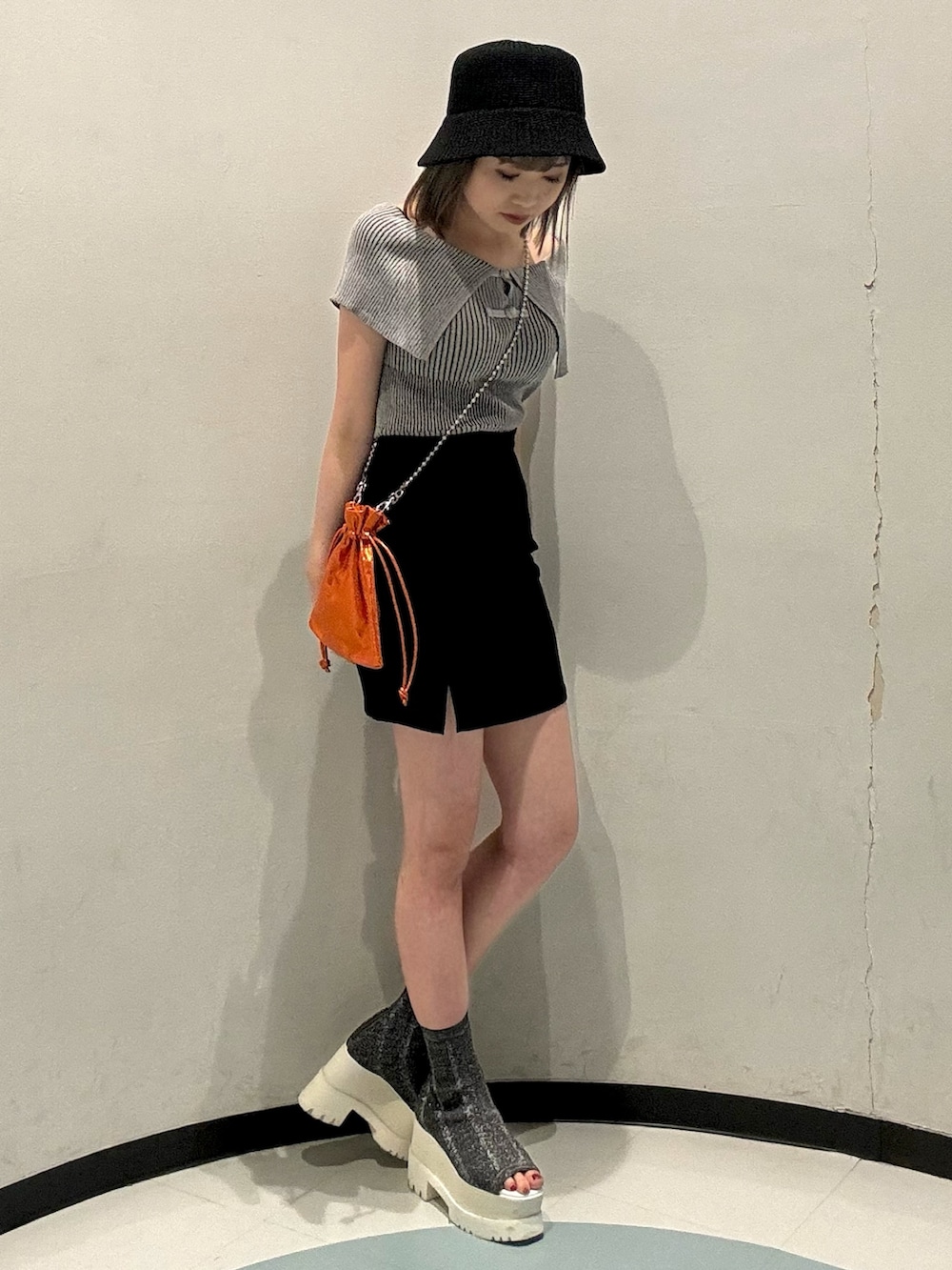 グレー系のニット/セーター、ブラック系のスカート、オレンジ系のショルダーバッグを着用したレディースの春コーディネートの2枚目の写真