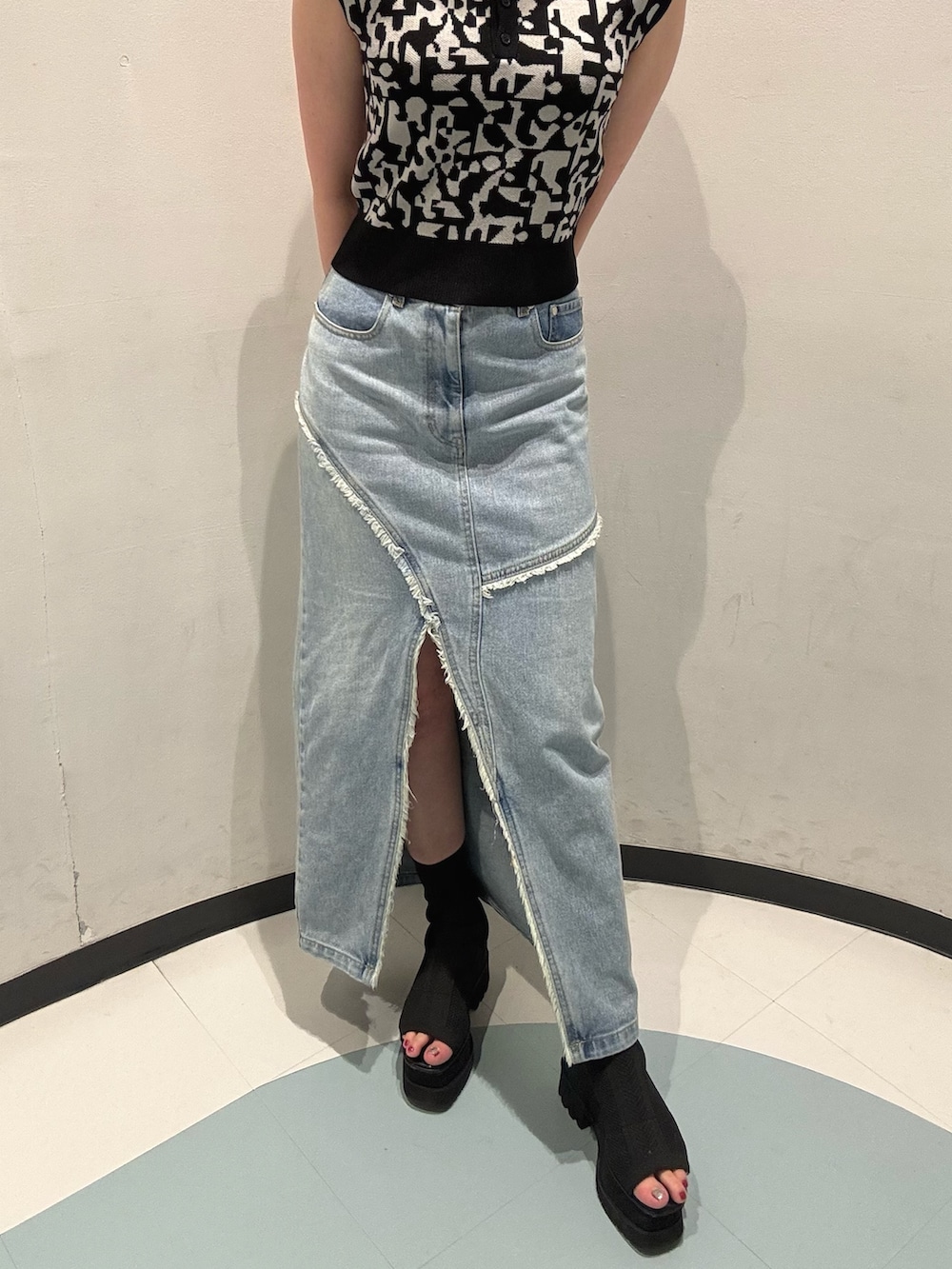 ブラック系のニット/セーター、ブルー系のデニムスカート、ブラック系のサンダルを着用したレディースの夏コーディネートの6枚目の写真