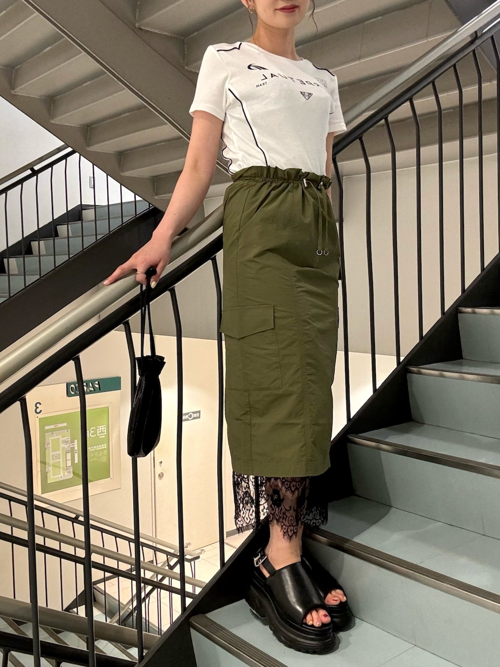 ホワイト系のTシャツ/カットソー、グリーン系のスカート、ブラック系のサンダルを着用したレディースの夏コーディネートの3枚目の写真