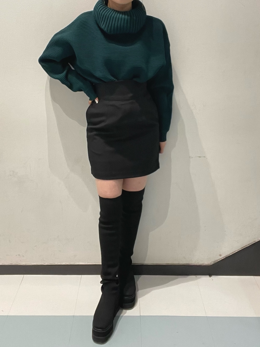 グリーン系のニット/セーター、ブラック系のブーツ、ブラック系のスカートを着用したレディースの秋コーディネートの2枚目の写真