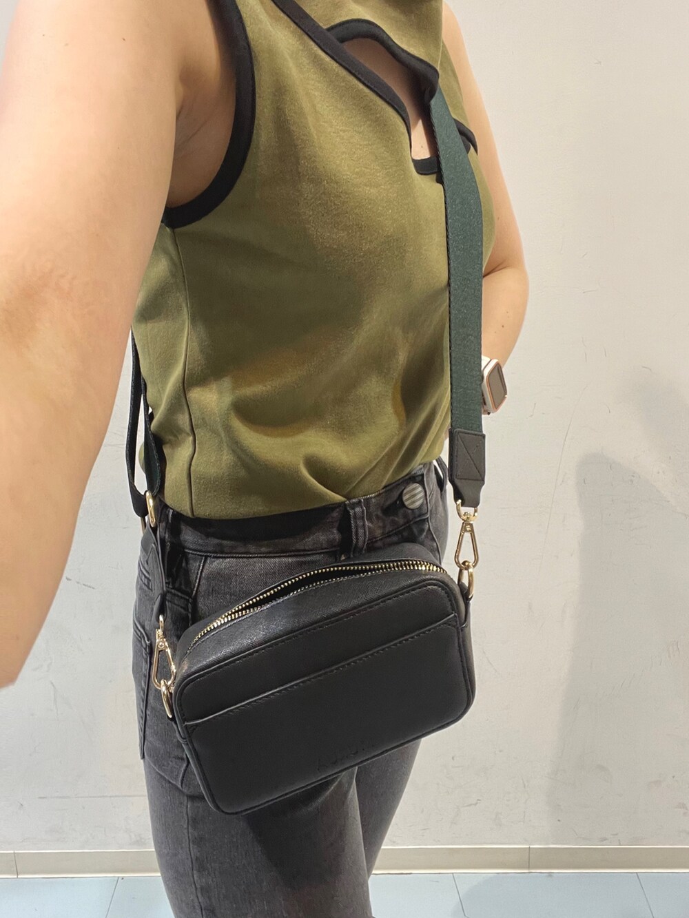 ブラック系のショルダーバッグ、グリーン系のタンクトップ、グレー系のデニムパンツを着用したレディースの夏コーディネートの5枚目の写真