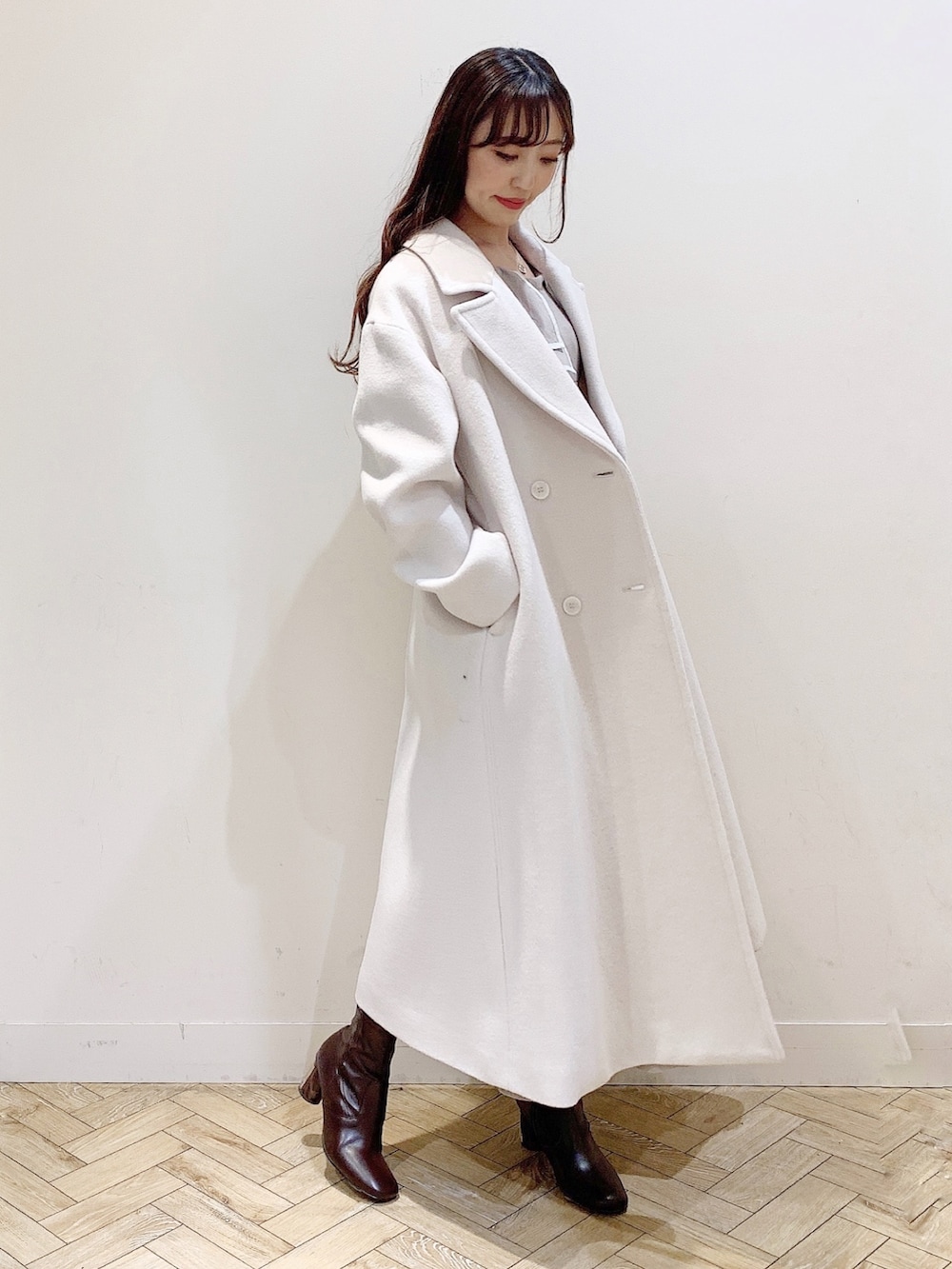 ベージュ系のワンピース、ホワイト系のチェスターコート、ブラウン系のブーツを着用したレディースの冬コーディネートの7枚目の写真