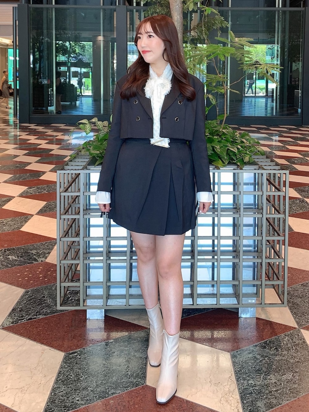 ブラック系のスカート、ブラック系のテーラードジャケット、ベージュ系のブーツを着用したレディースの秋コーディネートの2枚目の写真