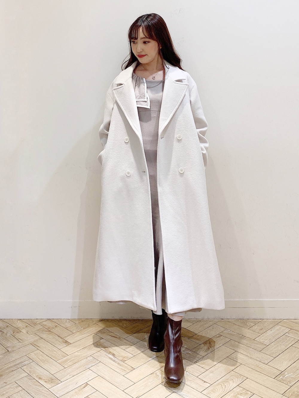 ベージュ系のワンピース、ホワイト系のチェスターコート、ブラウン系のブーツを着用したレディースの冬コーディネートの6枚目の写真