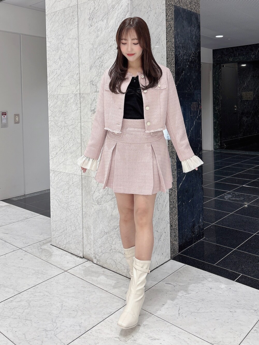 ピンク系のノーカラージャケット、ピンク系のスカート、ホワイト系のブーツを着用したレディースの冬コーディネートの2枚目の写真