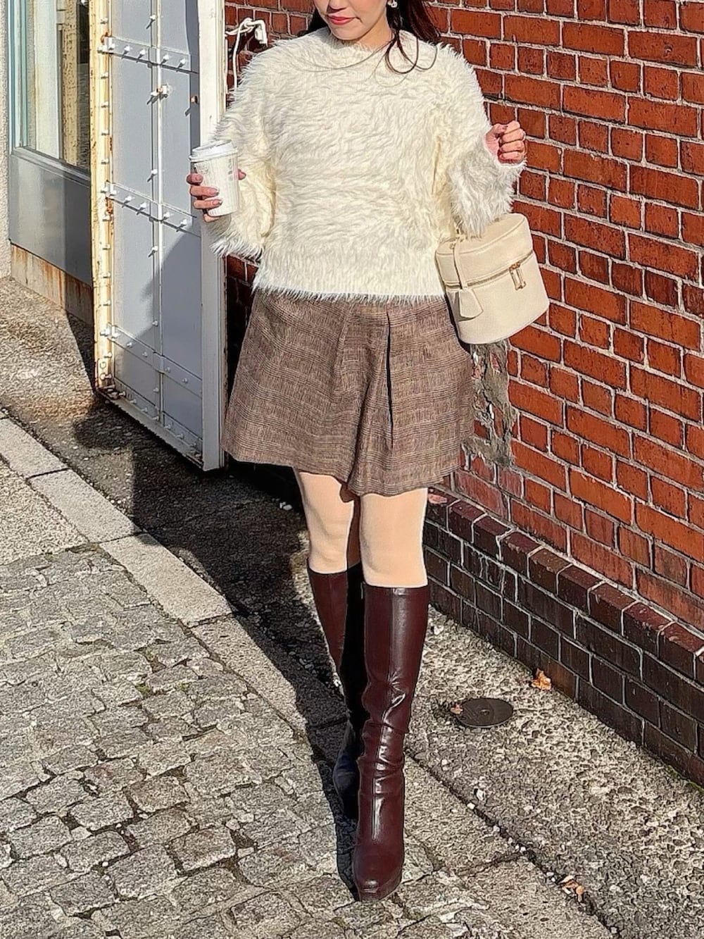 ホワイト系のニット/セーター、ブラウン系のスカートを着用したレディースの冬コーディネートの2枚目の写真