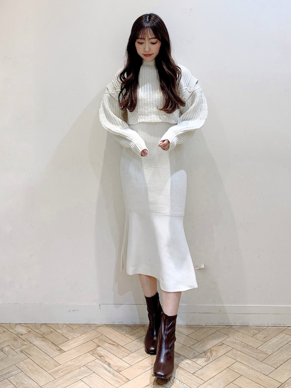 ホワイト系のワンピース、ベージュ系のステンカラーコート、ブラウン系のブーツを着用したレディースの冬コーディネートの2枚目の写真