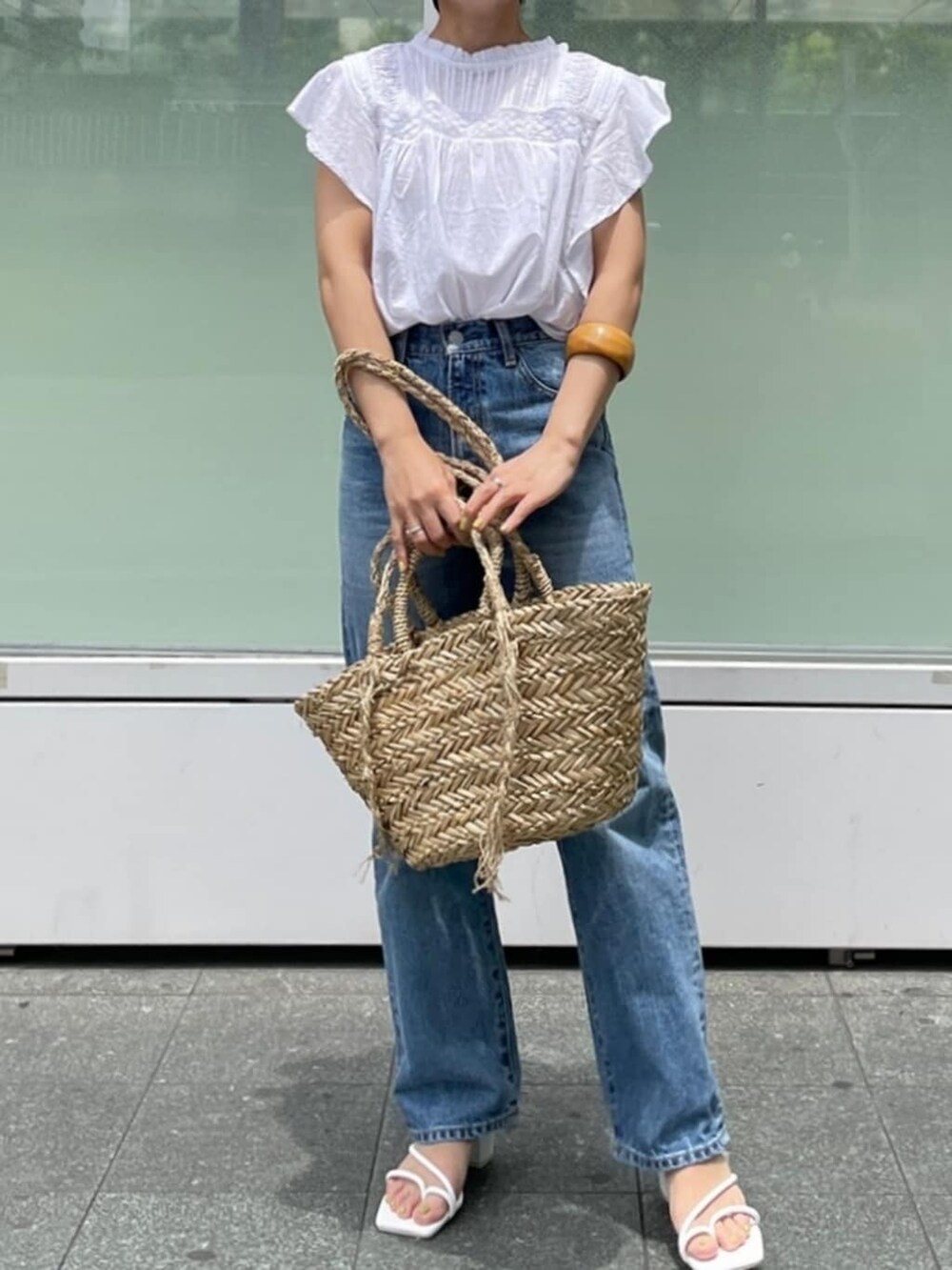 ブルー系のデニムパンツ、ベージュ系のかごバッグ、ホワイト系のシャツ/ブラウスを着用したレディースの夏コーディネートの2枚目の写真