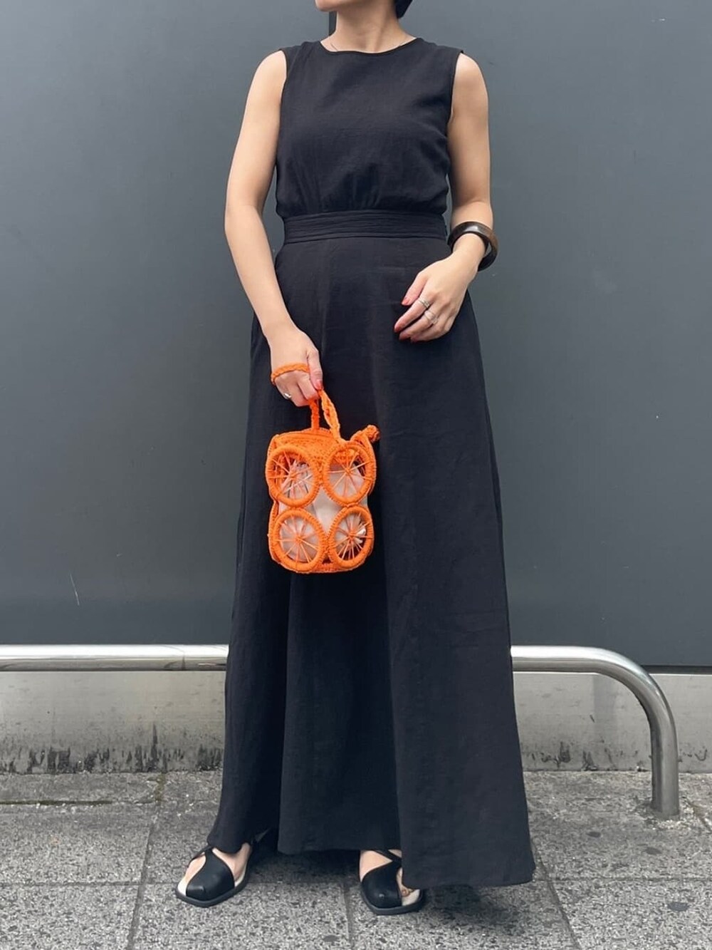 オレンジ系のかごバッグ、ブラック系のサンダル、ブラック系のタンクトップを着用したレディースの春コーディネートの2枚目の写真