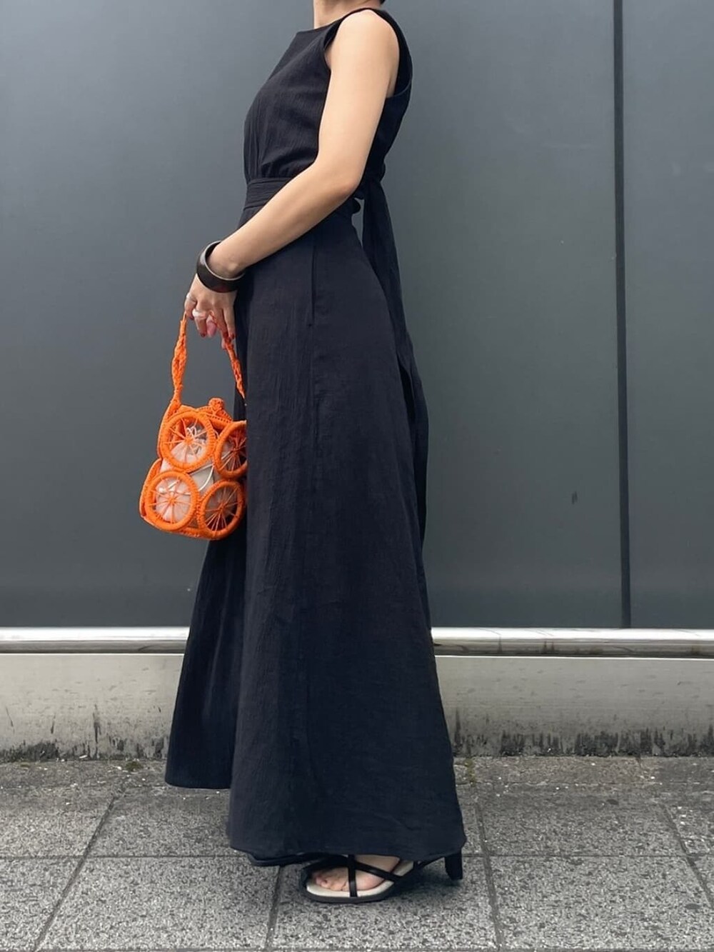 オレンジ系のかごバッグ、ブラック系のサンダル、ブラック系のタンクトップを着用したレディースの春コーディネートの3枚目の写真