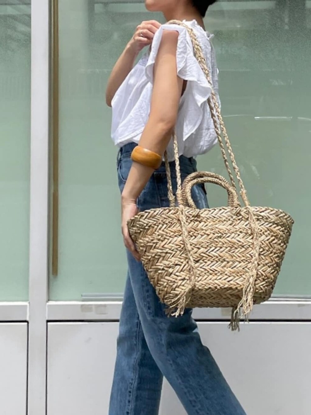 ブルー系のデニムパンツ、ベージュ系のかごバッグ、ホワイト系のシャツ/ブラウスを着用したレディースの夏コーディネートの3枚目の写真